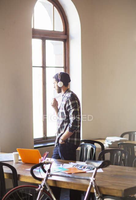 Pensativo empresario creativo con auriculares mirando por la ventana de la oficina - foto de stock