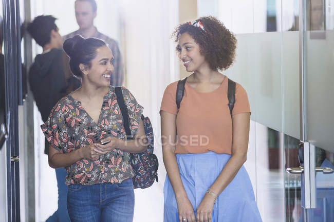 Sonrientes estudiantes universitarias caminando por el pasillo - foto de stock