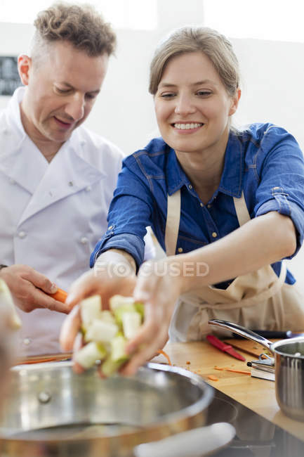 Mujer colocando comida en olla en cocina de clase de cocina - foto de stock