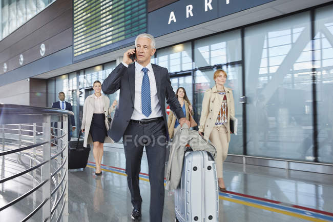 Uomo d'affari che parla al cellulare spingendo valigia nella hall dell'aeroporto — Foto stock