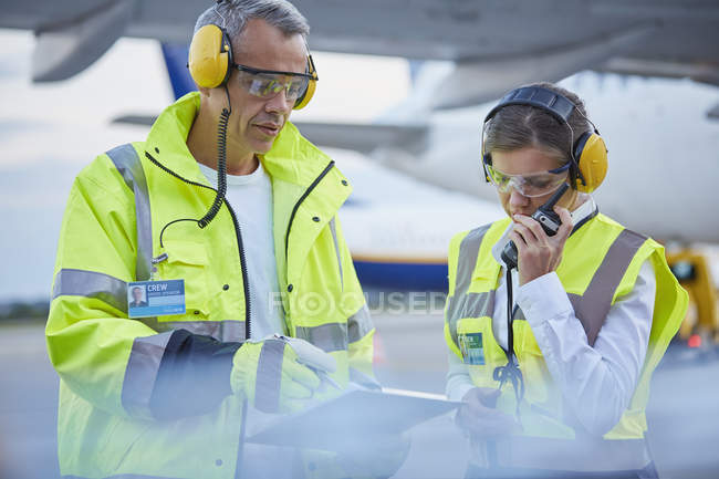 Trabajadores de la tripulación de tierra de control de tráfico aéreo con portapapeles hablando en asfalto del aeropuerto - foto de stock