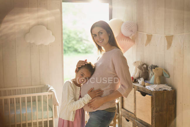 Retrato sonriente madre embarazada e hija en la guardería - foto de stock