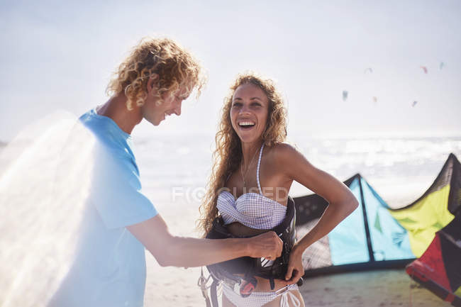 Homem fixando chicote de segurança kiteboarding na mulher na praia ensolarada — Fotografia de Stock