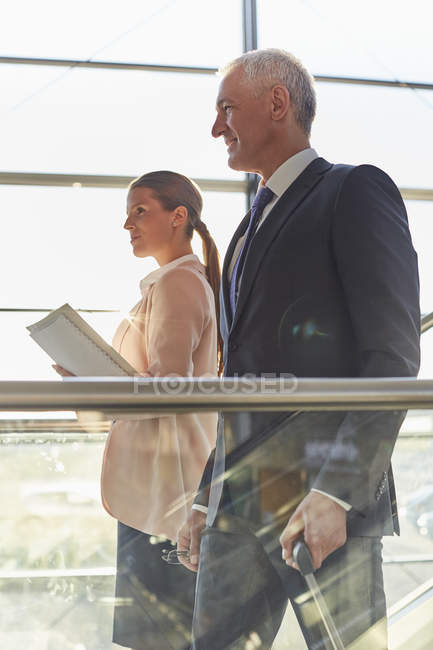 Hombre de negocios sonriente en escaleras mecánicas en el aeropuerto - foto de stock