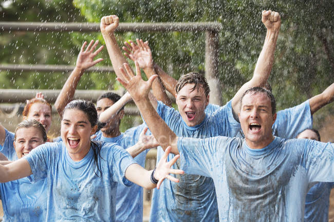 Enthusiastic team cheering in rain on boot camp obstacle course — Stock Photo
