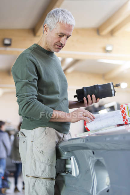 Mechanic with part reviewing instructions in auto repair shop — Stock Photo