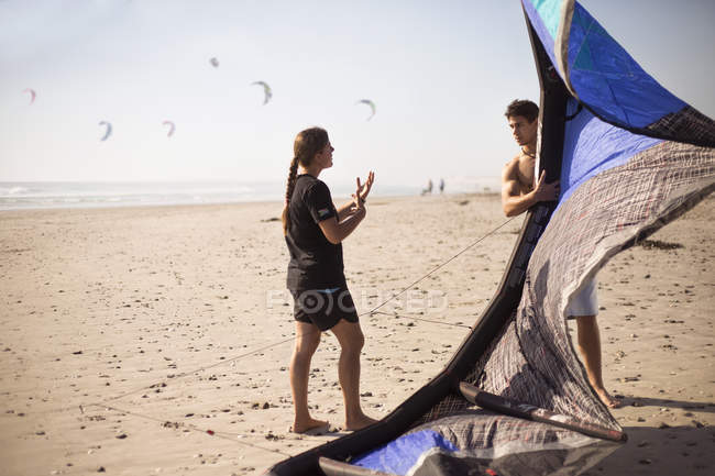 Mujer instruyendo hombre con kitesurf cometa en la playa soleada - foto de stock