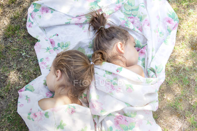 Twin girls napping in floral sheet on grass — Stock Photo