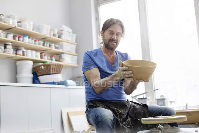 Portrait confident mature man holding bowl at pottery wheel in studio — Stock Photo