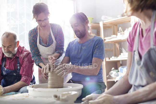 Teacher guiding mature man at pottery wheel in studio — Stock Photo