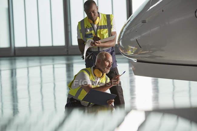 Airport ground crew workers examining airplane in hangar — Stock Photo