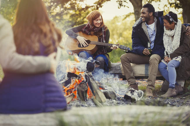 Friends playing guitar and drinking beer at campfire — Stock Photo