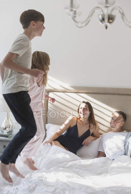 Eltern beobachten Kinder beim Springen im Bett — Stockfoto