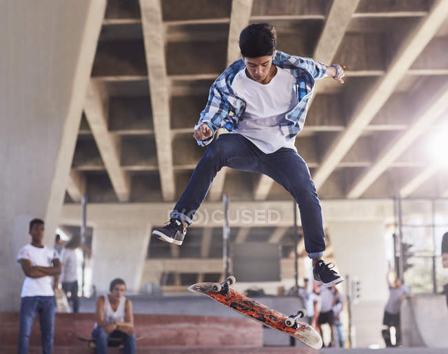 Friends watching teenage boy flipping skateboard at skate park — Stock Photo
