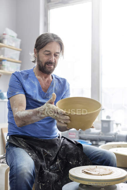 Mature man holding bowl at pottery wheel in studio — Stock Photo