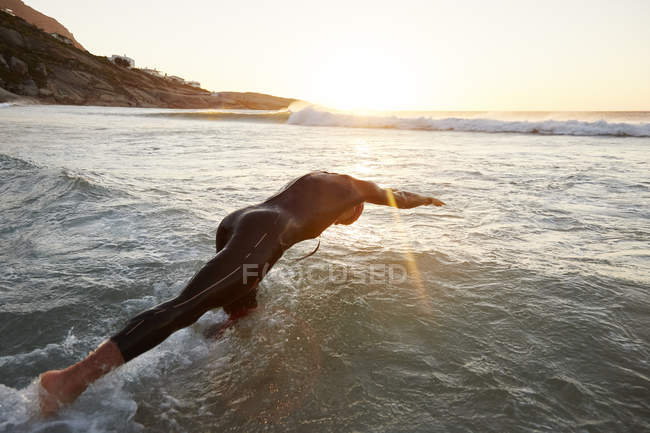 Чоловічий тріатлоніст плаває у мокрій костюмі, занурюючись у океан — стокове фото