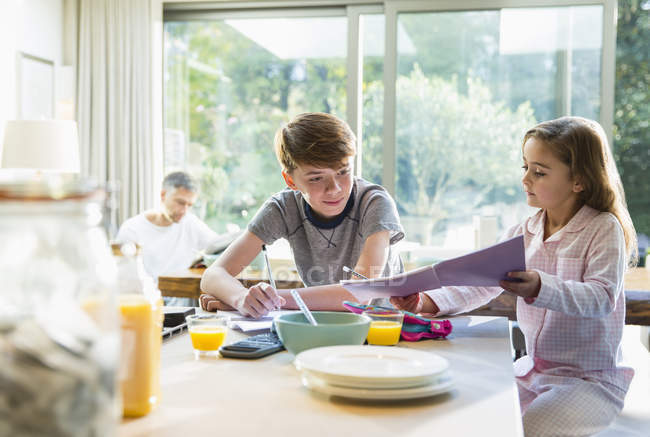 Brother and sister eating breakfast and doing homework — Stock Photo