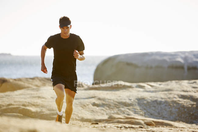 Triatleta masculino correndo em trilha rochosa ensolarada — Fotografia de Stock