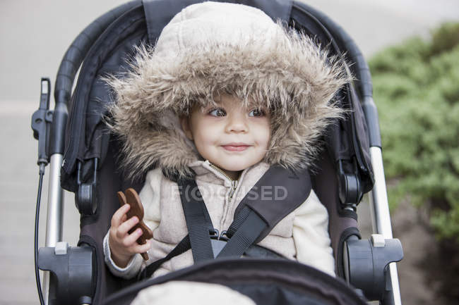 Smiling girl in fur hood riding in stroller — Stock Photo