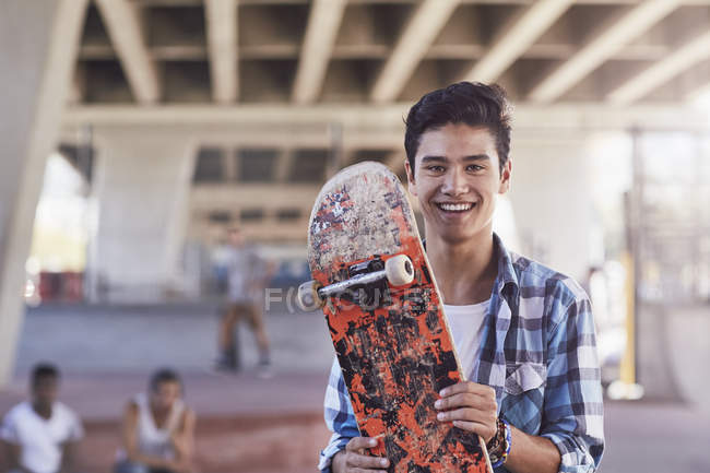 Portrait smiling teenage boy holding skateboard at skate park — Stock Photo
