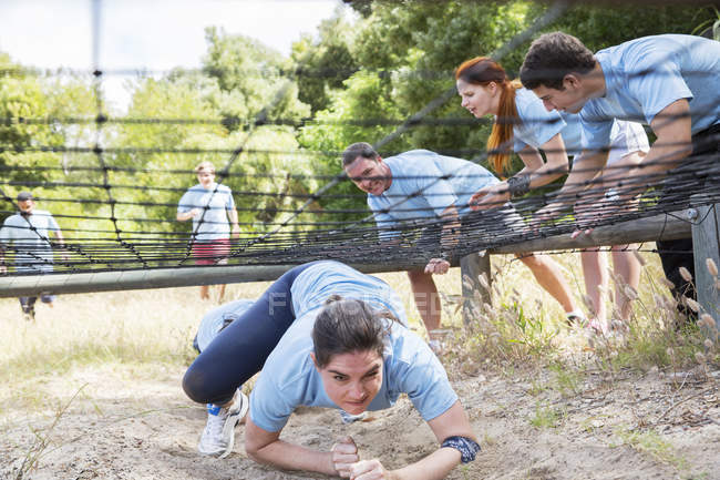 Determinada mujer arrastrándose bajo la red en el campo de entrenamiento carrera de obstáculos - foto de stock
