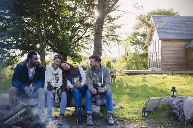 Friends drinking beer relaxing at campfire outside cabin — Stock Photo