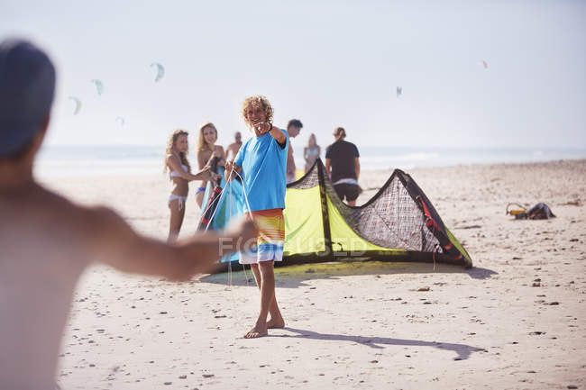 Amigos preparando kitesurf en la playa soleada - foto de stock