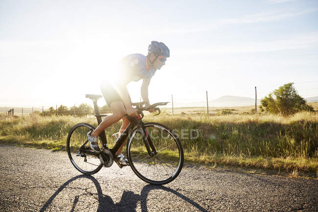 Triatleta ciclista masculino ciclista na estrada rural ensolarada ao nascer do sol — Fotografia de Stock