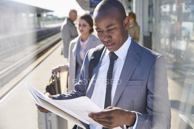 Бізнесмен читає документи на платформі сонячної залізничної станції — стокове фото
