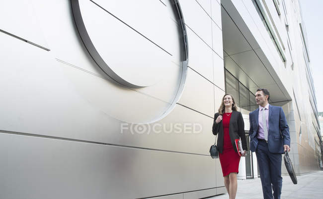 Корпоративный бизнесмен и деловая женщина, выходящие за пределы современного здания — стоковое фото