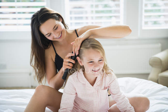 Madre cepillando el pelo de la hija en la cama - foto de stock