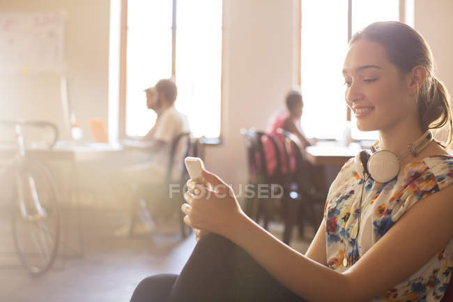 Усміхнений випадковий бізнес-леді смс на мобільний телефон в офісі — стокове фото