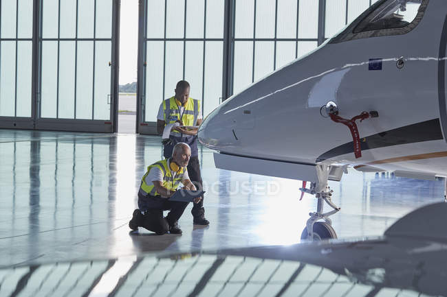 Air traffic control ground crew workers examining corporate jet in airplane hangar — Stock Photo