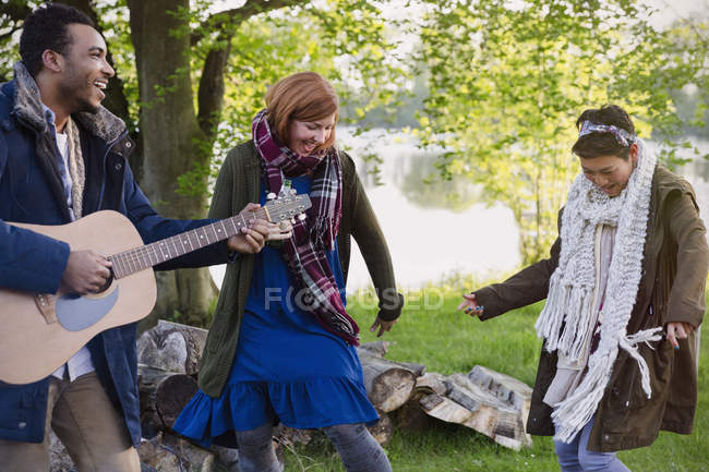Amigos tocando la guitarra y bailando en el camping junto al lago - foto de stock