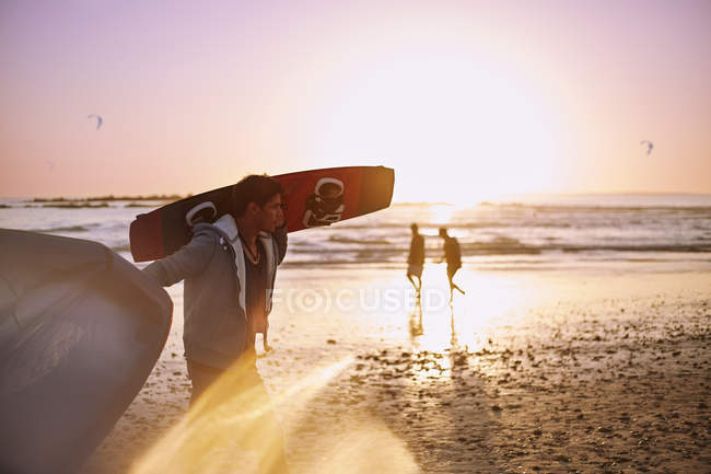 Uomo che trasporta kiteboard sulla spiaggia del tramonto — Foto stock