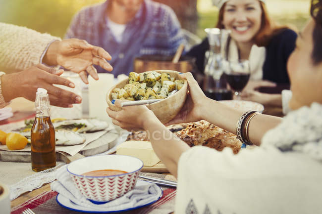 Friends passing food across patio lunch table — Stock Photo