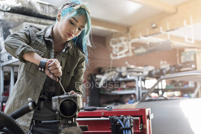 Jeune mécanicien femelle avec partie de réparation de cheveux bleus dans l'atelier de réparation automobile — Photo de stock