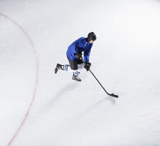 Хоккеист в синей форме катается на коньках с шайбой на льду — стоковое фото