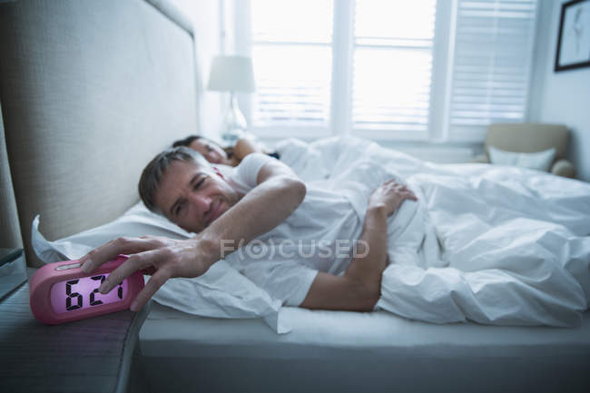 Uomo a letto spegnere sveglia mattutina — Foto stock