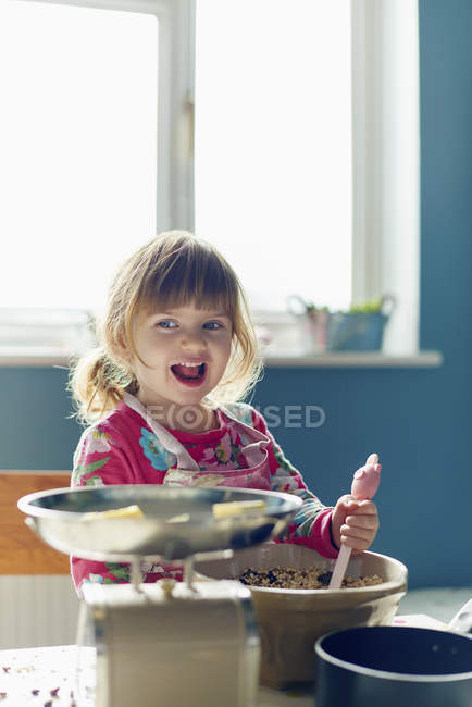 Chica sonriente hornear con tazón de mezcla en la cocina - foto de stock