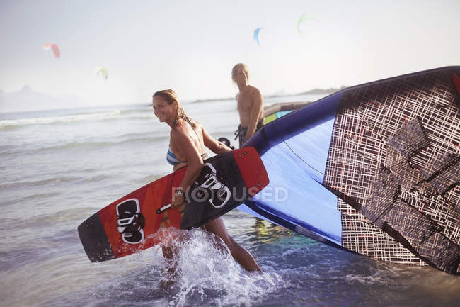 Couple pulling kiteboarding equipment into ocean surf — Stock Photo