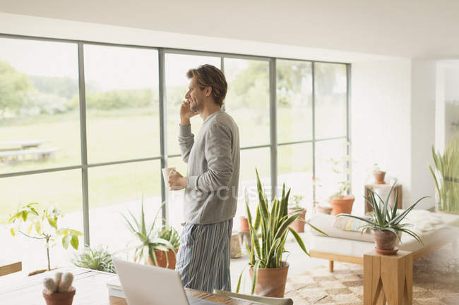 Чоловік у піжамі розмовляє на мобільному телефоні та п'є каву — стокове фото