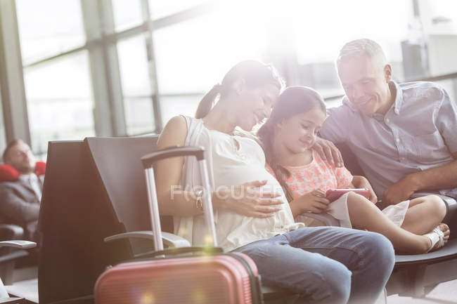 Вагітна сім'я використовує цифровий планшет, який чекає в зоні відправлення аеропорту — стокове фото
