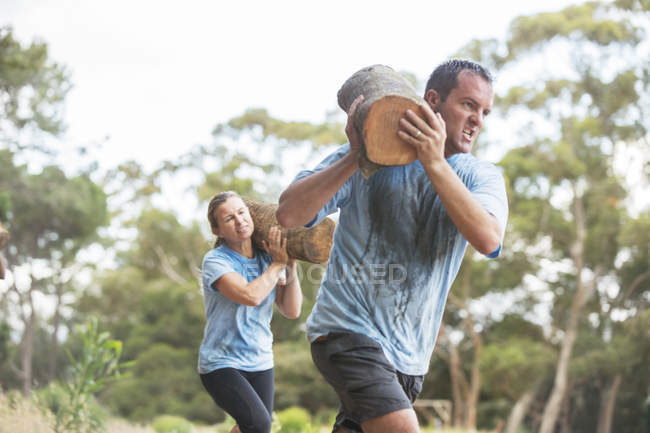 Homem e mulher correndo com logs no campo de treinamento — Fotografia de Stock