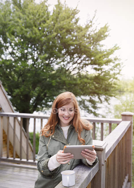 Smiling woman with red hair using digital tablet on cabin balcony — Stock Photo