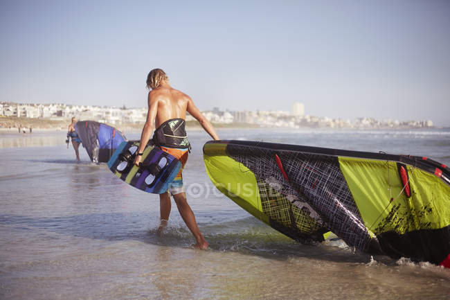 Man dragging kiteboarding equipment into ocean surf — Stock Photo