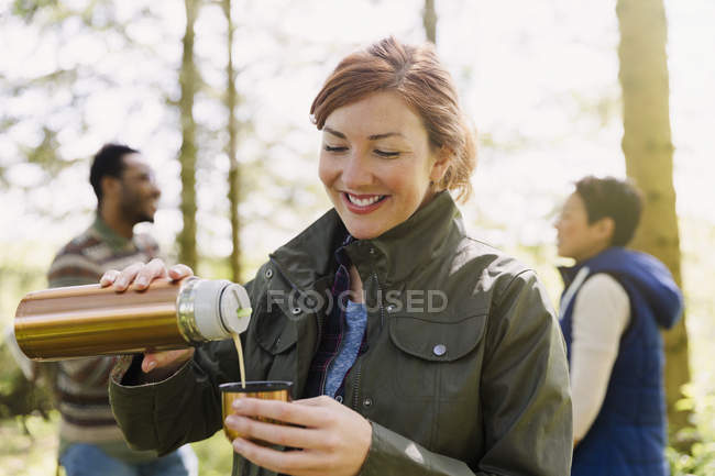 Smiling woman pouring coffee from insulated drink container in woods — Stock Photo