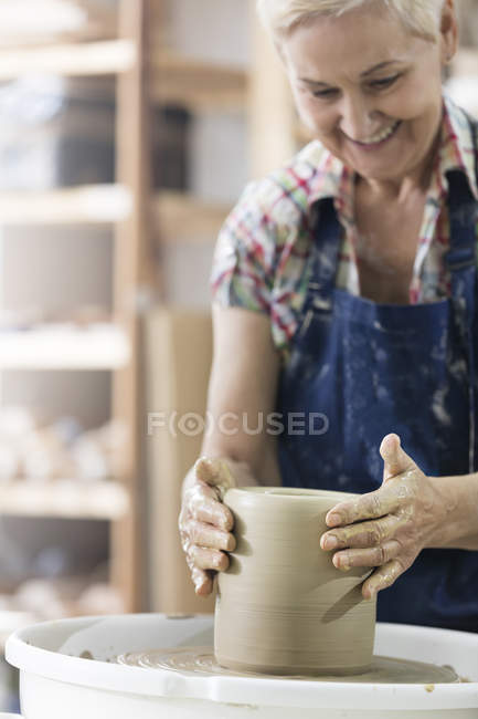 Mujer mayor sonriente usando rueda de cerámica en el estudio - foto de stock