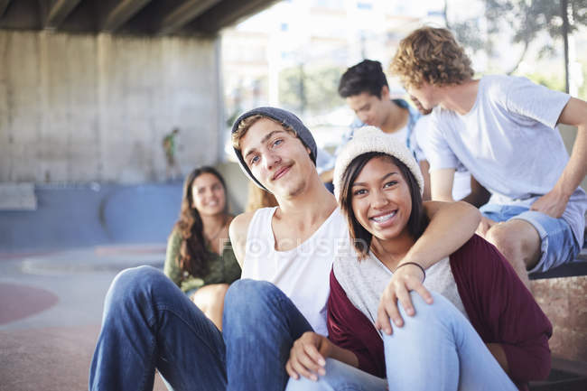 Портрет улыбающейся подростковой пары, тусующейся с друзьями в скейт-парке — стоковое фото