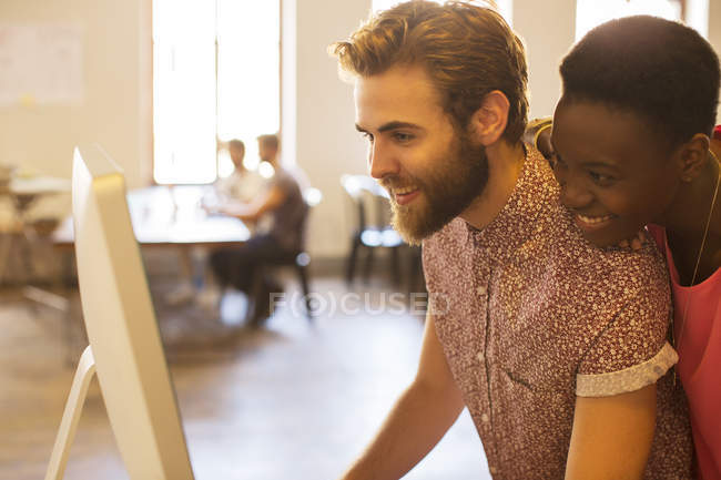 Smiling casual business people sharing computer in office — Stock Photo